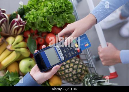 Femme qui paie des articles d'épicerie à l'aide de sa carte de crédit, la caissière du supermarché tient le terminal du PDV Banque D'Images