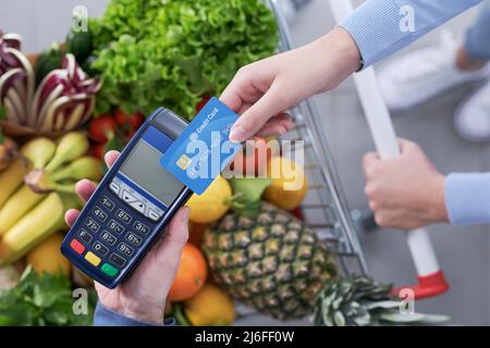 Femme qui paie des articles d'épicerie à l'aide de sa carte de crédit, la caissière du supermarché tient le terminal du PDV Banque D'Images