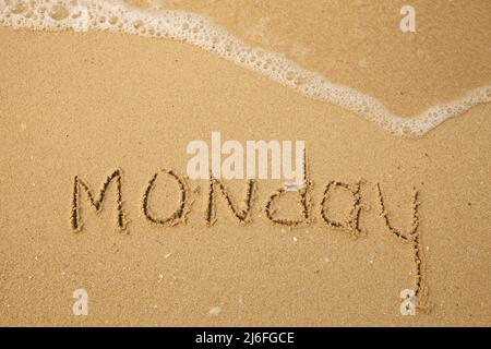 Lundi - manuscrit sur le sable léger de la plage avec une vague douce de lapping. Banque D'Images