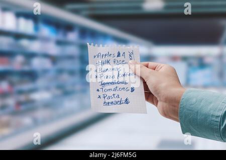 Femme tenant une liste de magasinage manuscrite et une allée de supermarché en arrière-plan Banque D'Images