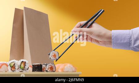 Femme mangeant des sushis à l'aide de baguettes et d'un sac de livraison de nourriture en arrière-plan Banque D'Images