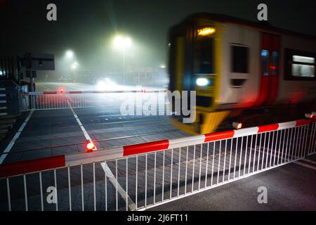 Un train en mouvement sur un passage à niveau automatique à Barmouth, dans le nord du pays de Galles, par une nuit brumeuse Banque D'Images