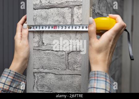 une femme utilisant un mètre à ruban mesure une saillie sur le mur. Photo de haute qualité Banque D'Images