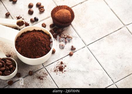 Fond de café. Cuillères à mesurer avec du café moulu, des haricots, une tasse et des truffes au chocolat doux sur un fond de table vieux carrelage fissuré. La nourriture. Banque D'Images