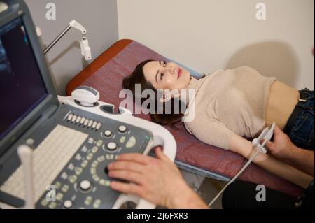 Une belle patiente se trouve sur un lit médical lors d'un examen dans la salle de diagnostic échographique. Radiologie, bilan médical, soins de santé et Banque D'Images