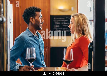 couple multiethnique discutant au bar du restaurant tout en buvant du vin rouge Banque D'Images