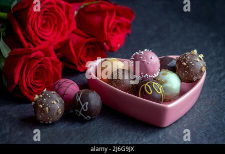 une délicieuse variété de truffes au chocolat dans un plat de bonbons à coeur rose, avec des roses rouges Banque D'Images