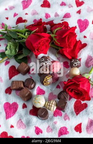 les roses et les chocolats sont exposés sur un fond romantique de coeurs rouges et roses Banque D'Images