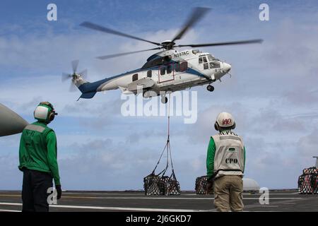 MER DES PHILIPPINES (7 avril 2022) Spécialiste en logistique, le marin Joel Elizee, à gauche, de Golpsboro, N.C., Et le spécialiste en chef de la logistique Willie Bates, d'Elizabethtown, Ky., observe un fret de transport Super Puma AS332 sur le pont de vol du porte-avions de la classe Nimitz USS Abraham Lincoln (CVN 72) lors d'un réapprovisionnement vertical en mer avec le navire de fret et de munitions sec USNS Richard E. Byrd (T-AKE 4). Abraham Lincoln Strike Group est en cours de déploiement prévu dans la zone d'exploitation de la flotte américaine 7th afin d'améliorer l'interopérabilité par le biais d'alliances et de partenariats Banque D'Images