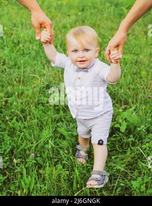 La main des parents et l'enfant première étape.Bébé jouant dans l'herbe verte.Enfant s'amusant sur un pique-nique en famille dans le jardin d'été.Portrait d'une jeune famille heureuse Banque D'Images