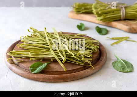 Pâtes brutes fettuccine avec des épineuses sur une planche à découper en bois et un fond en béton Banque D'Images