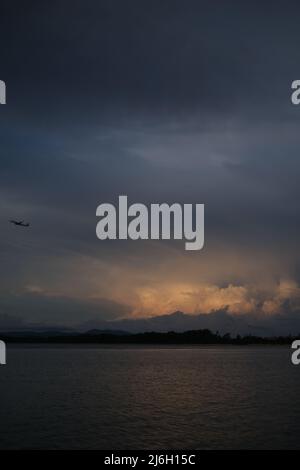 Un avion monte au-dessus de la mer après le décollage, devant un nuage d'orage isolé éclairé par le soleil couchant Banque D'Images
