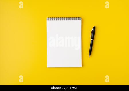 Carnet spirale vierge avec stylo plume sur fond jaune coloré, vue de dessus, recopie Banque D'Images