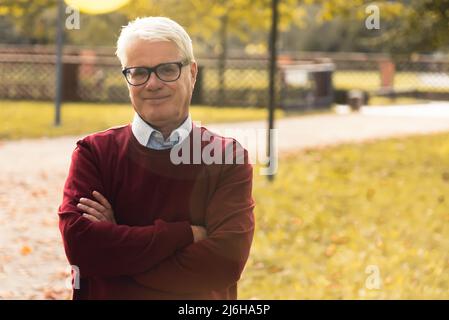 Contenu Homme européen senior en chandail rouge debout dans le parc. Concept de retraite et de vitalité. Photo de haute qualité Banque D'Images
