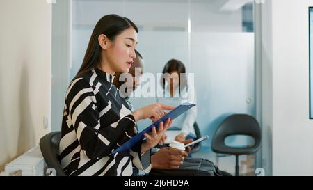 Femme asiatique regardant le cv et se préparant à l'entrevue d'emploi, attendant de commencer la réunion sur le recrutement et la sélection. Le candidat se sent nerveux et lit les dossiers dans la file d'attente. Banque D'Images