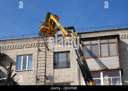 Élévateur articulé diesel près du toit d'un bâtiment de plusieurs étages. Travaux de réparation sur le toit par les services municipaux. Ascenseur en métal jaune. Banque D'Images