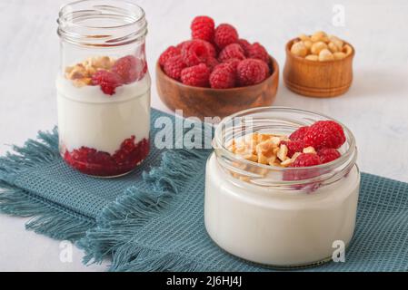 Alimentation saine, yaourt grec ordinaire, framboises fraîches et noisettes écrasées sur fond blanc. Banque D'Images