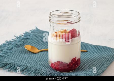 Alimentation saine, yaourt grec ordinaire, framboises fraîches et noisettes écrasées sur fond blanc. Banque D'Images