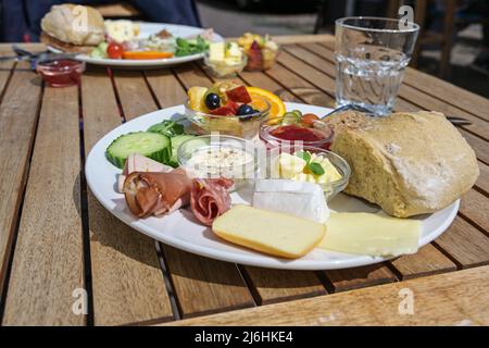 Petit déjeuner varié ou assiette déjeuner dans un restaurant de rue avec saucisse et jambon, petits pains, fromage et fruits sur une table extérieure en bois par beau temps, Banque D'Images