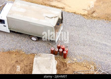 Un petit camion avec un auvent sur la carrosserie se tient sur un chantier de construction près de plusieurs bouteilles de gaz rouge - propane, concentration sélective Banque D'Images