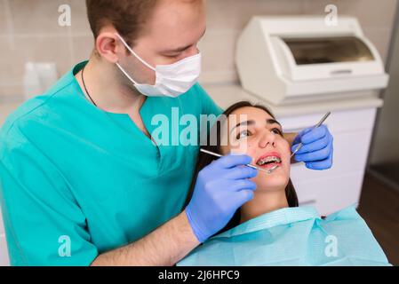 Un dentiste de sexe masculin examine les dents d'un patient à l'aide d'un microscope dentaire professionnel. Le client est sur la chaise du dentiste Banque D'Images