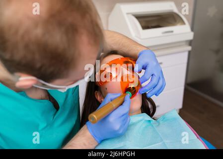 Une patiente en lunettes dentaires traite les dents du dentiste à la lumière ultraviolette. Plombages dentaires Banque D'Images