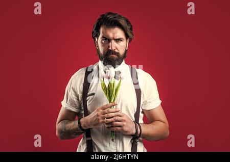 élégant homme brutal en tenue formelle a les cheveux soignés tenir des fleurs de tulipe, jour des femmes Banque D'Images