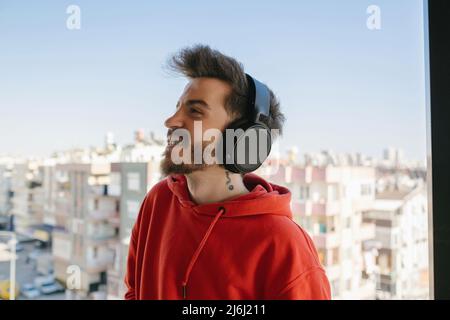 Casque d'écoute, sweat-shirt rouge avec casque et écouter de la musique sur le balcon, écouter de la musique et profiter de l'instant Banque D'Images