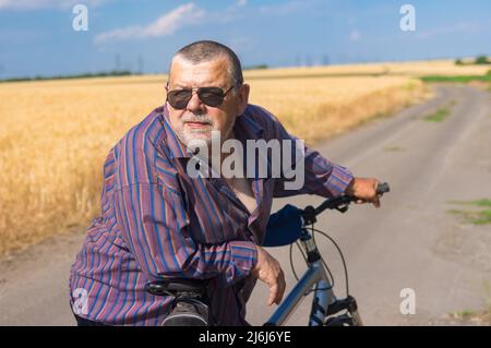 Portrait extérieur d'un homme ukrainien barbu et corsé se pencha sur les coudes pour prendre la barre de son vélo lors d'un court repos sur un parcours d'été dans un pays Banque D'Images