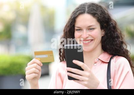 Bonne femme achetant en ligne avec carte de crédit et téléphone cellulaire dans la rue Banque D'Images