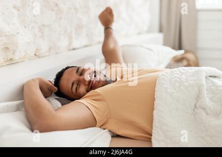 Joyeux arabe Homme réveissant bâilling bras allongé dans la chambre Banque D'Images