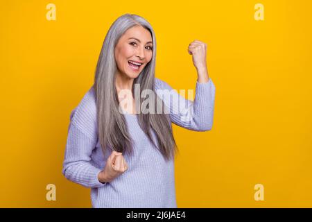 Photo de gai overjoyed riant mûr femme élever les poings dans la victoire devenir millionnaire gagner l'argent isolé sur fond jaune de couleur Banque D'Images