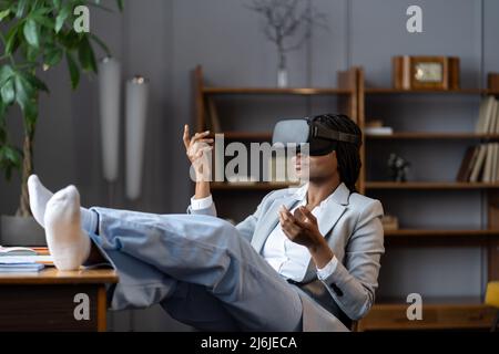 Femme afro détendue dans un micro-casque VR méditant en réalité virtuelle sur le lieu de travail pendant les pauses Banque D'Images
