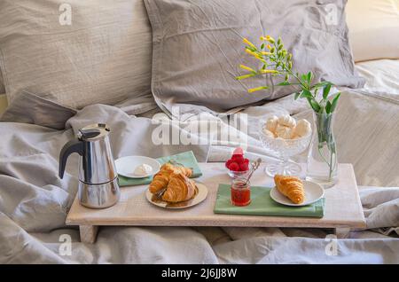 Petit-déjeuner romantique ou un brunch pour deux au lit. Cafetière et café verres, des croissants, de la confiture, des fruits rouges, meringue et fleurs sur bois romantique. Banque D'Images