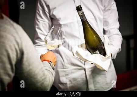 garçon avec chemise blanche sert du vin mousseux à un client, des emplois et de l'artisanat Banque D'Images