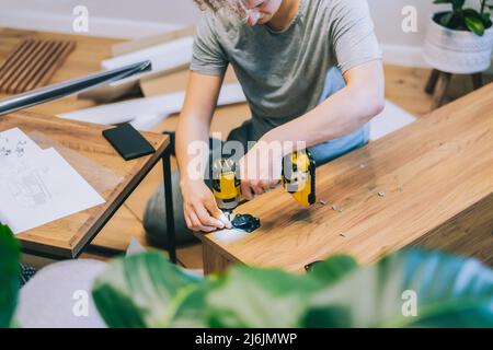 Un jeune homme avec un tournevis électrique assemble une console de support de tv selon les instructions dans sa nouvelle maison. Homme assemblant des meubles à la maison u Banque D'Images