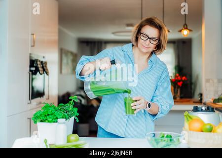 Femme d'âge moyen versant de la boisson de détox, smoothie vert du mélangeur dans le verre à la cuisine maison. Manger, manger et cuisiner sainement. Anti-âge naturel moi Banque D'Images