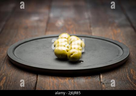 Grandes olives vertes sur une assiette noire sur une table en bois Banque D'Images