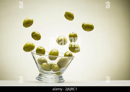 Grandes olives vertes sautant hors du bol en verre, sur fond coloré Banque D'Images