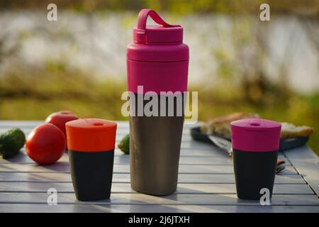 Un ensemble d'ustensiles de camping est placé sur une table pliante dans la nature. Conteneurs de liquides touristiques Banque D'Images