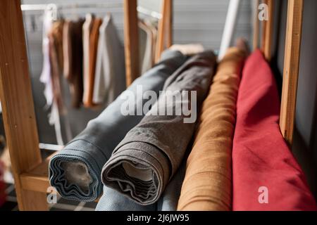 Pile de rouleaux de plusieurs textiles naturels de différentes couleurs sur étagère en bois dans un entrepôt moderne spacieux ou atelier de tailleur Banque D'Images