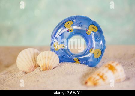 Cercle de natation décoratif et coquillages de mer restant dans le sable.bon comme arrière-plan pour la superposition de texte. Banque D'Images