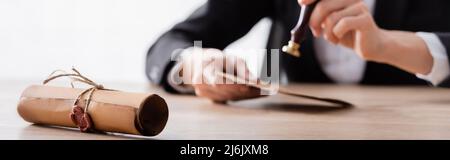 vue rognée de l'enveloppe d'estampage de notaire floue près du parchemin roulé avec sceau de cire, bannière Banque D'Images