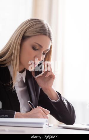 notaire blond parlant sur téléphone portable et écrivant au bureau Banque D'Images