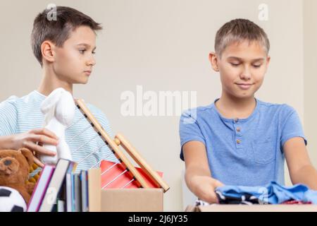 Boîte de dons. Les enfants bénévoles trient des jouets, des vêtements, des livres, des fournitures de papeterie dans des boîtes de dons de charité. Banque D'Images