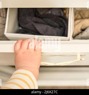 Bébé garçon se déporte d'un tiroir de cabinet avec sa main. L'enfant tient la poignée de la porte de l'armoire, petit enfant Banque D'Images