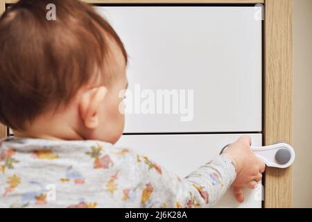 Bébé garçon se déporte d'un tiroir de cabinet avec sa main. L'enfant tient la poignée de la porte de l'armoire, petit enfant Banque D'Images