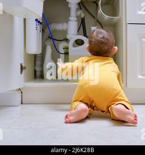 Bébé garçon joue avec des détergents et des produits de nettoyage dans une armoire de cuisine ouverte. Problèmes de sécurité des enfants dans la chambre d'accueil, petit enfant Banque D'Images