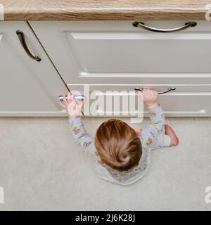 Bébé garçon se déporte d'un tiroir de cabinet avec sa main. L'enfant tient la poignée de la porte de l'armoire, petit enfant Banque D'Images