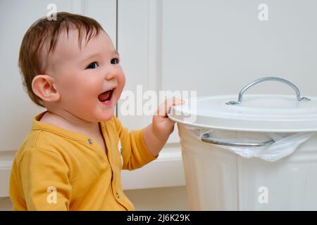 Bébé garçon ouvre une poubelle avec les déchets ménagers. Problèmes de sécurité des enfants dans la chambre d'accueil, petit enfant Banque D'Images